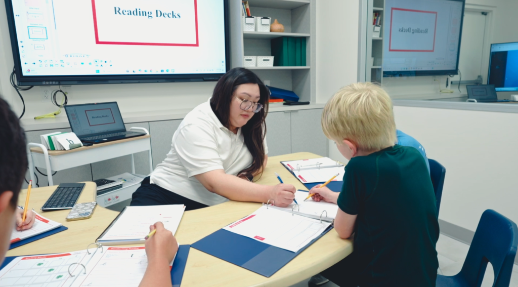 Teacher and student collaborating on a lesson while a touchscreen smartboard is in the background displaying lesson information